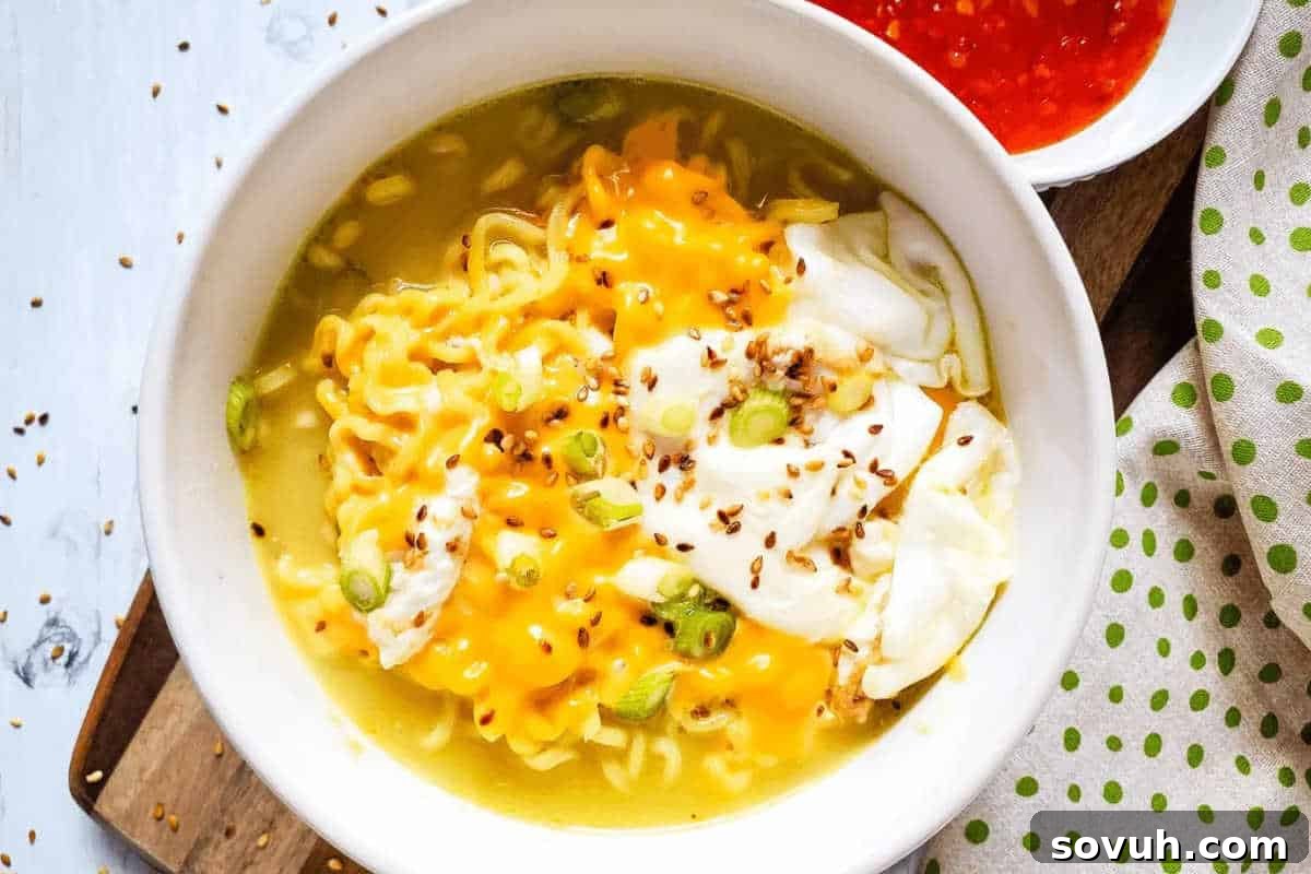 A comforting bowl of ramen soup, luxuriously topped with melted cheese, thinly sliced green onions, a sprinkle of sesame seeds, and a perfectly poached egg, with a side of red sauce visible in the background.