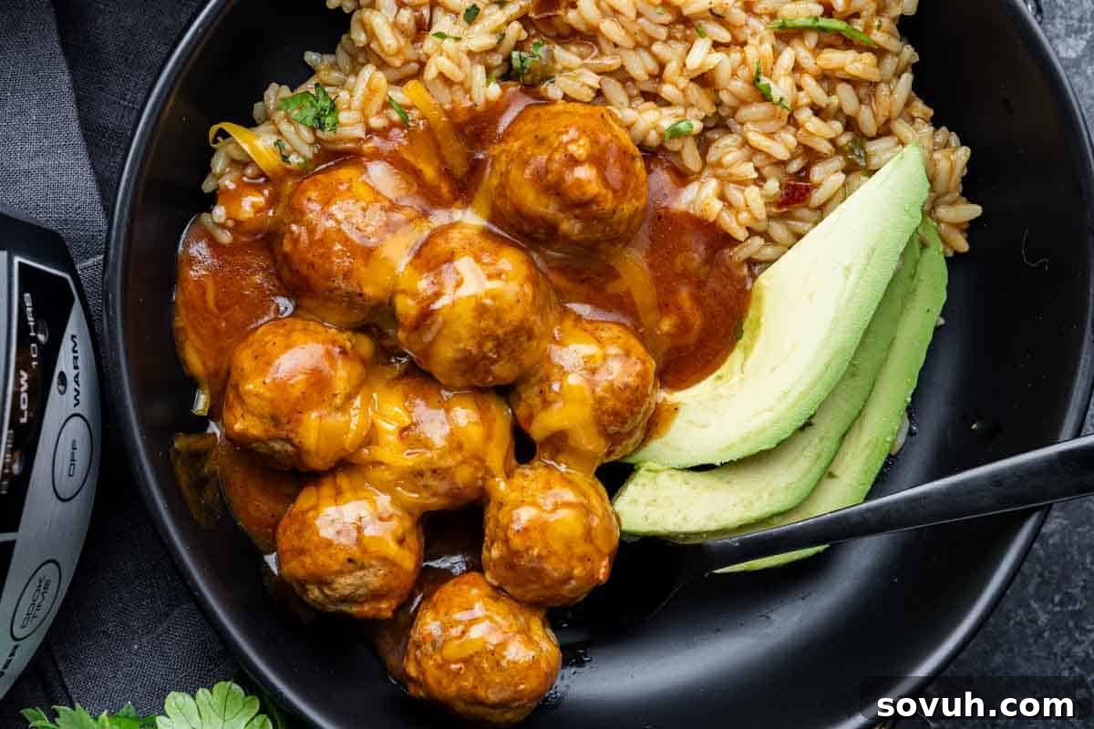A black bowl filled with saucy enchilada meatballs topped with melted cheese, served alongside fluffy rice and sliced avocado. A perfect illustration of a delicious and easy slow cooker meal.