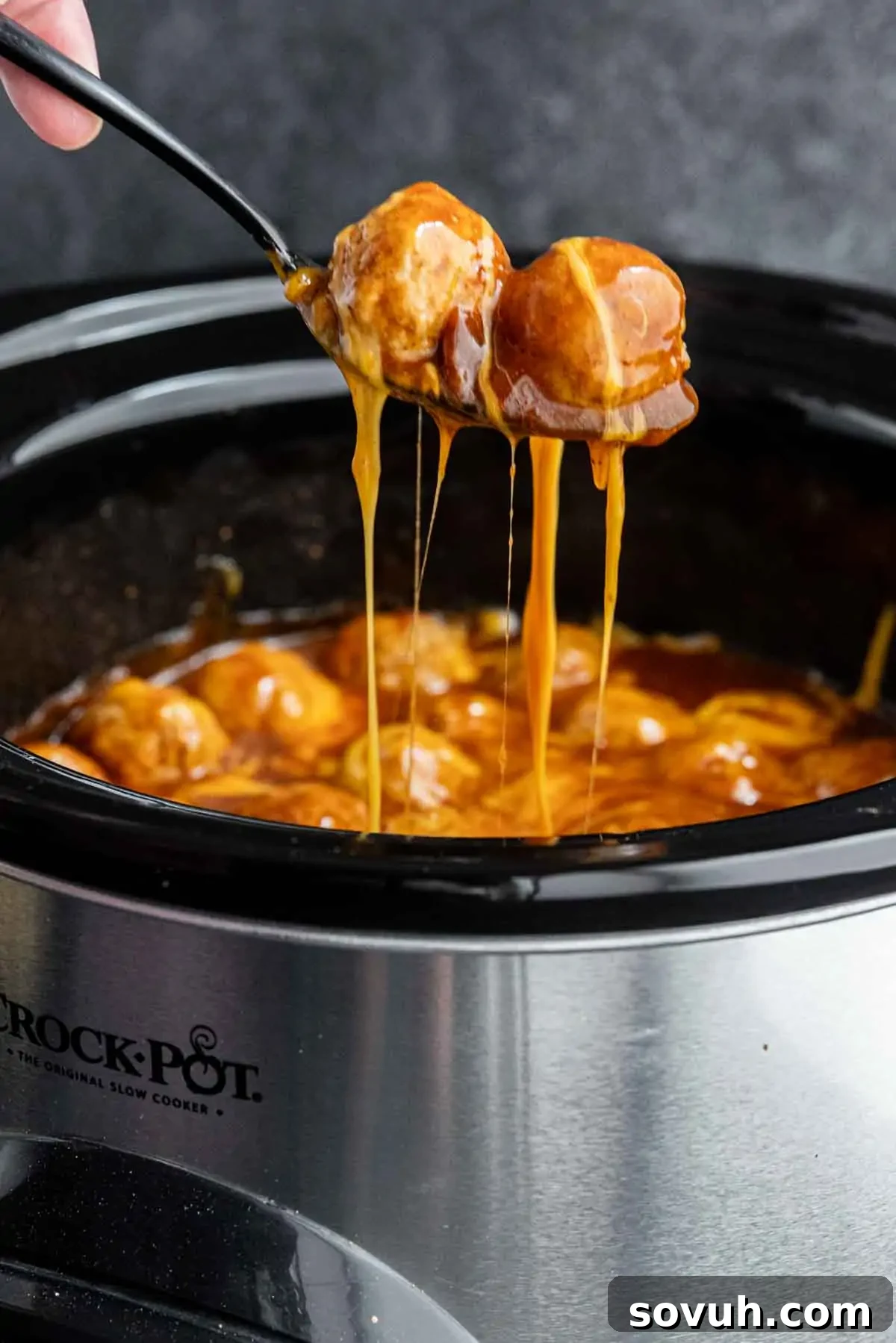 A serving spoon lifting a cluster of saucy, tender meatballs coated in a thick, rich enchilada glaze from a slow cooker, highlighting their irresistible texture.