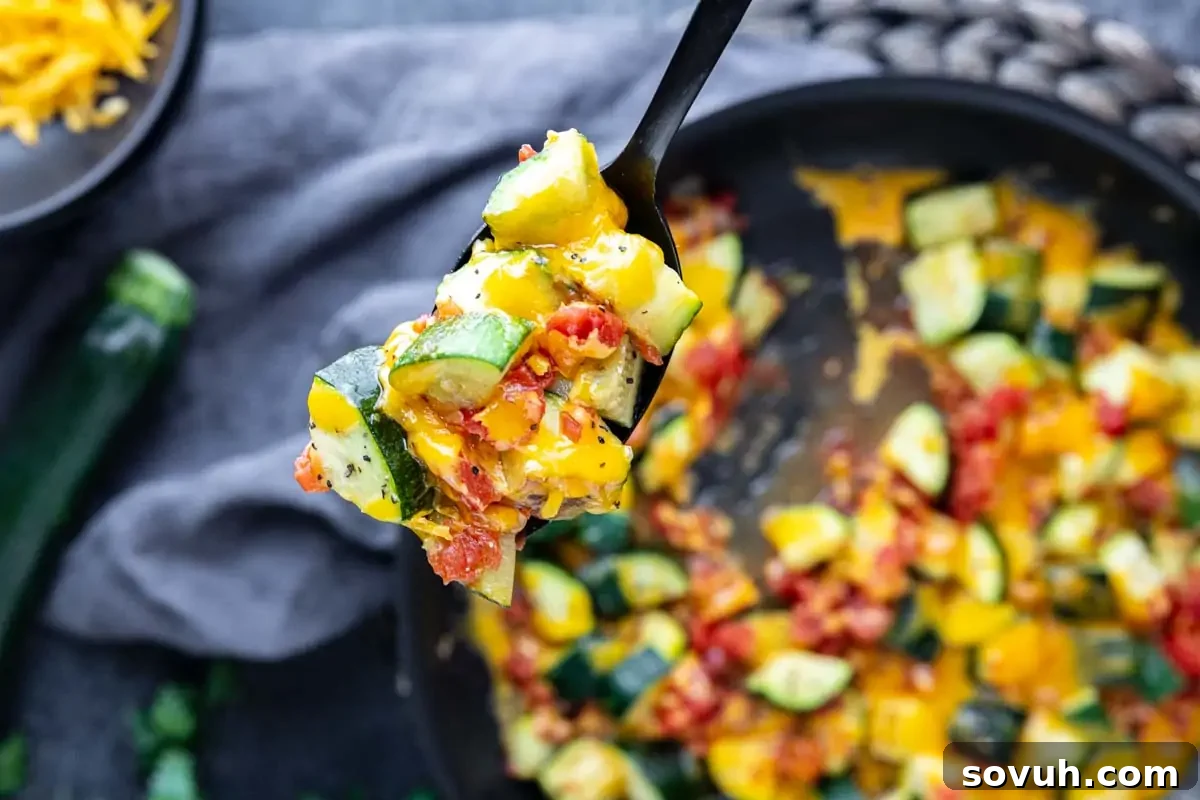 A close-up of a spoonful of perfectly cooked zucchini, vibrant diced tomatoes, and luscious melted cheese held over a rustic skillet filled with this savory mixture—a truly inspiring sight for hearty zucchini dishes and effortless summer meals.