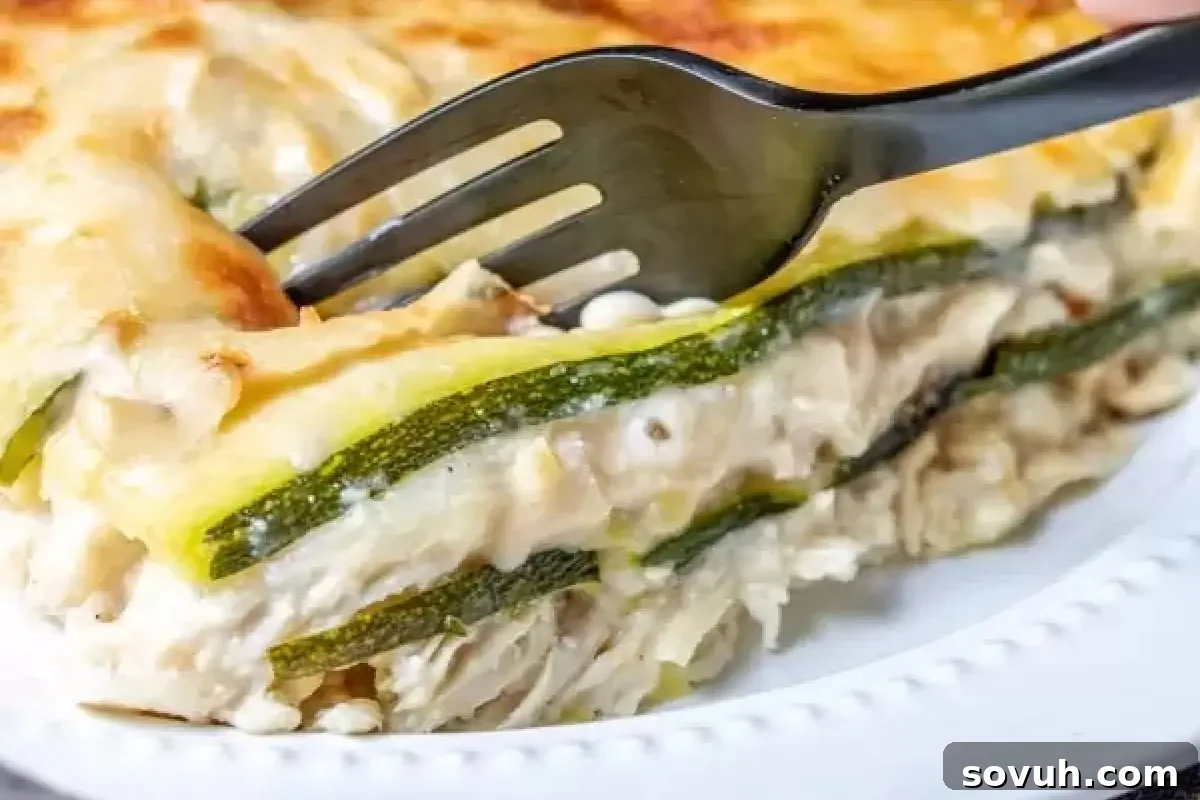 A close-up of a perfectly cut slice of zucchini lasagna, revealing luscious layers of tender zucchini, savory chicken, rich Alfredo sauce, and melted, golden cheese, showcasing one of the most creative and delicious zucchini recipes. A black fork gently presses into the top, highlighting this irresistible take on classic zucchini dishes.