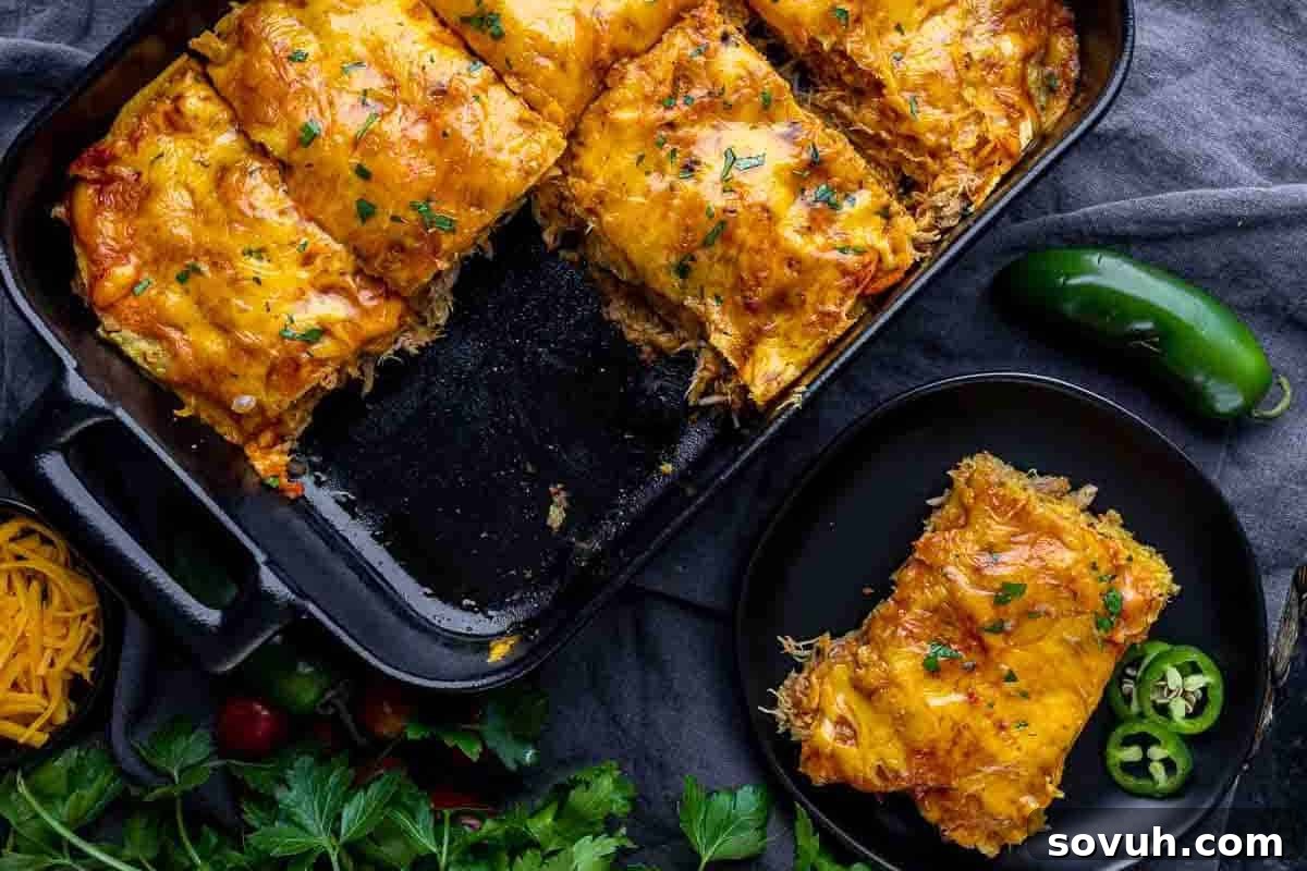 A casserole dish with cheesy baked enchilada casserole, one serving cut out and placed on a plate beside sliced jalapeños and fresh herbs.