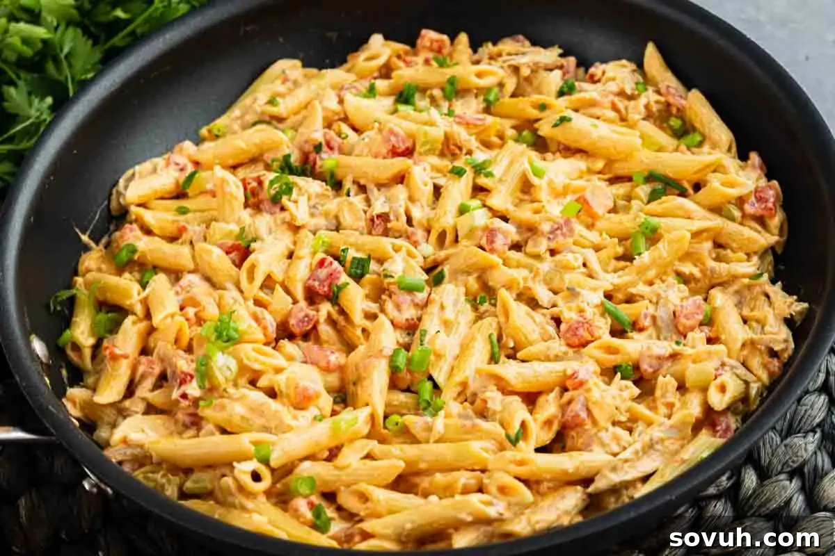 A skillet filled with creamy penne pasta mixed with diced tomatoes, herbs, and garnished with chopped green onions.