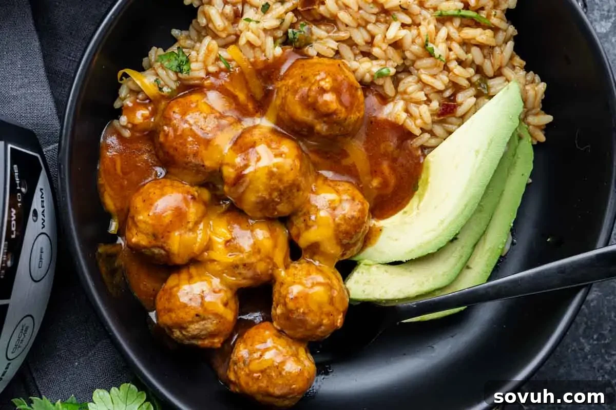 A black bowl with rice, sauced meatballs topped with melted cheese, and sliced avocado, with a black spoon on the side.