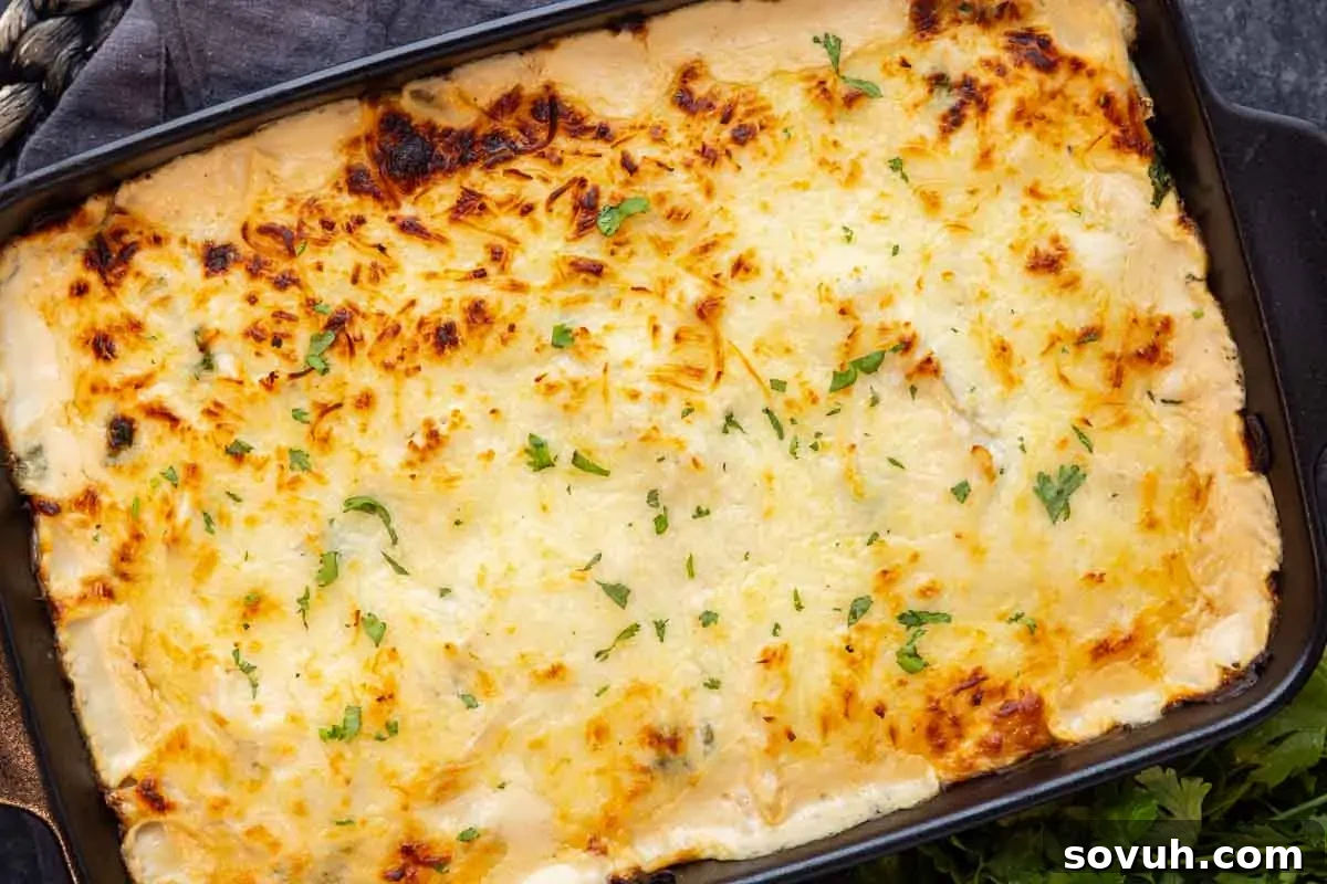 A baked casserole with a golden, cheesy crust, sprinkled with chopped parsley, in a rectangular dark dish.