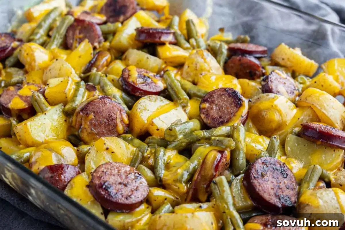 A baked dish with sliced sausage, yellow potatoes, green beans, and melted cheese in a glass baking pan.