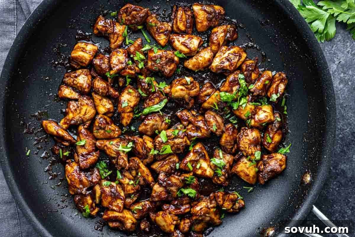 Cooked, browned pieces of chicken garnished with chopped parsley in a black skillet, set on a dark surface.