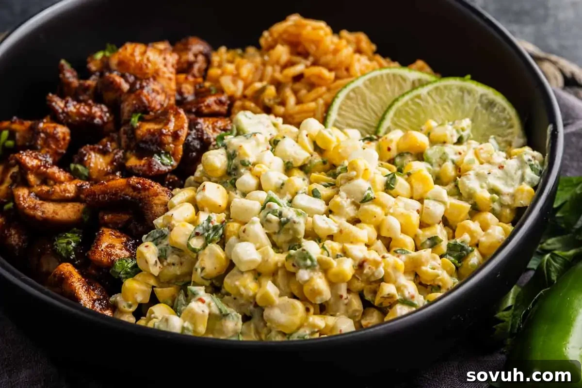 A bowl with seasoned grilled chicken, Mexican rice, creamy corn salad with herbs, and lime slices.