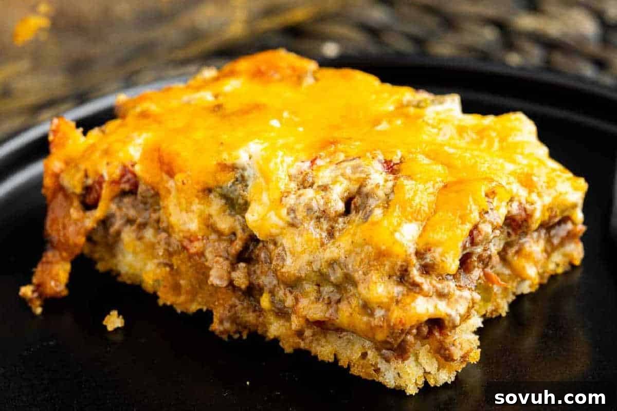 A slice of casserole on a black plate, featuring layers of ground meat, melted cheese, and a bread-like base.