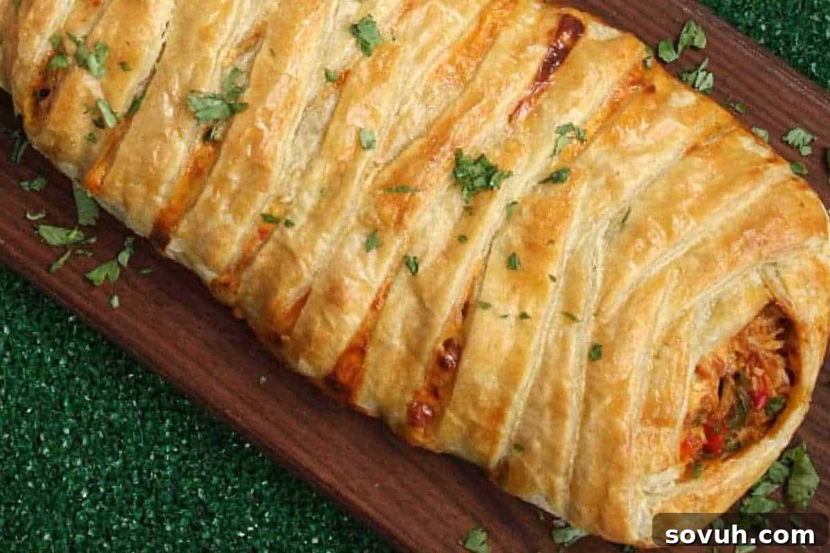 A golden-brown puff pastry filled with vegetables and meat, topped with chopped herbs, rests on a wooden board placed on a green surface.