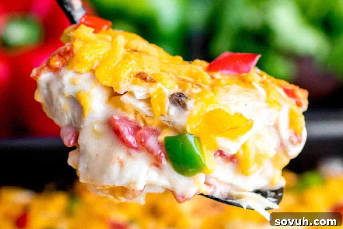 A close-up of a serving of creamy pasta bake with melted cheese, red and green bell peppers on a spatula.