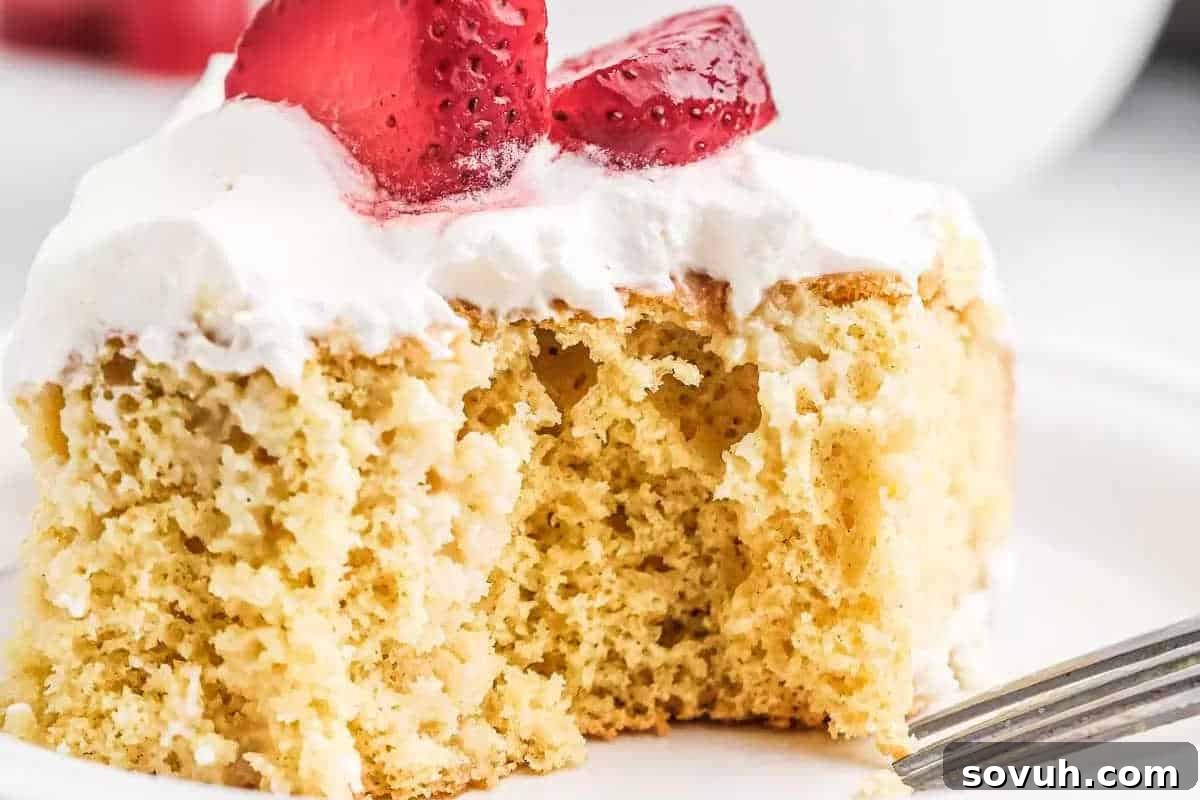 A slice of sponge cake with white frosting and sliced strawberries on top—perfect for those who love simple cooking and easy recipes—with a bite taken out and a fork resting nearby.