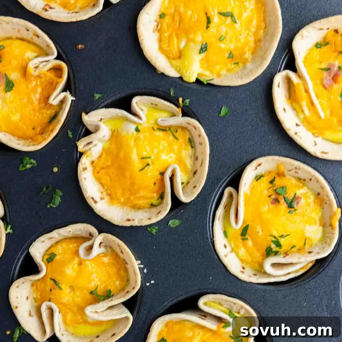 Mini tortilla cups filled with egg and melted cheese, garnished with chopped herbs, make these easy breakfast burrito cups a delicious start to your day. Arranged in a muffin tin for perfect breakfast burrito muffins every time.