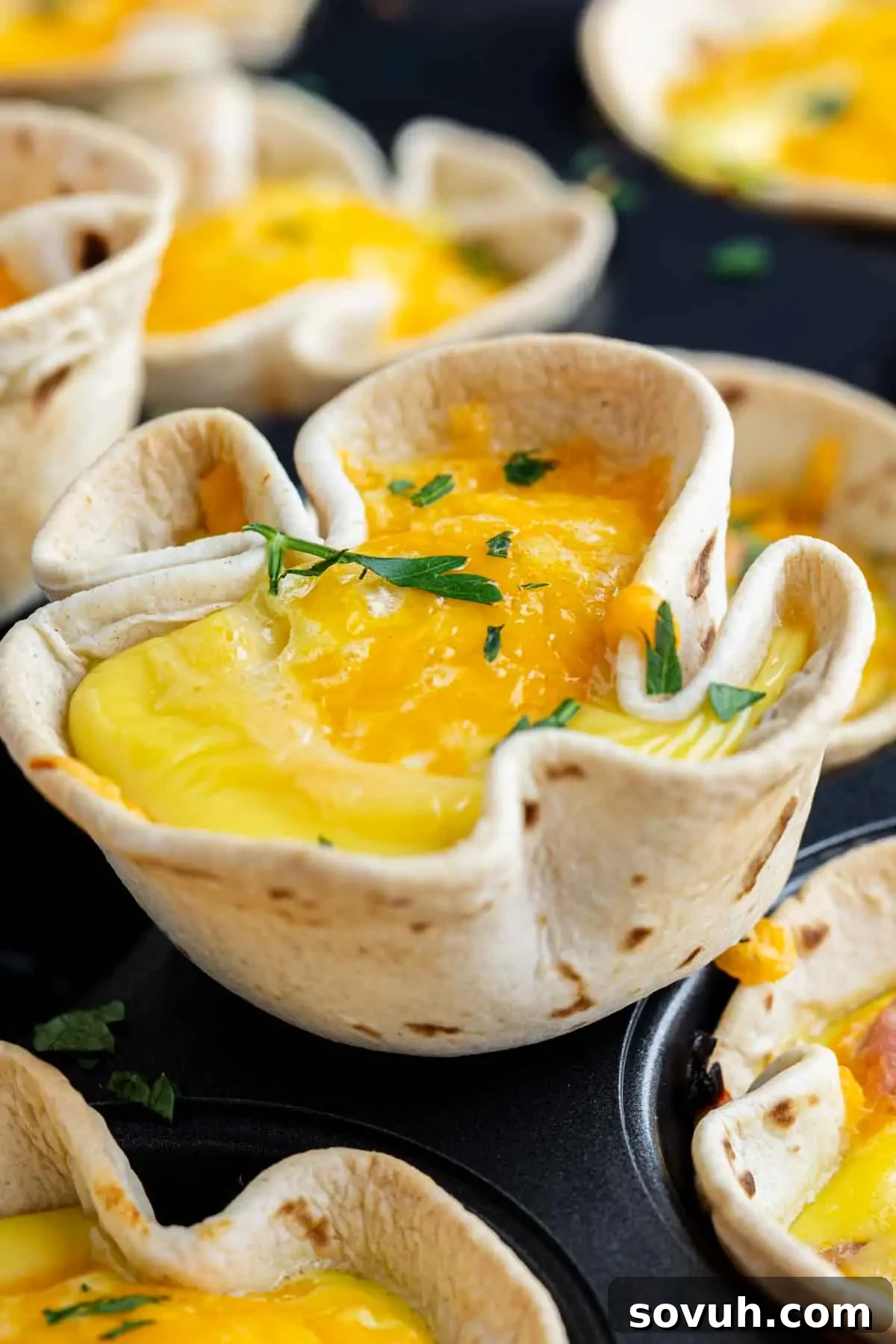 A close-up of easy breakfast burrito cups—baked tortilla cups filled with egg and melted cheese, garnished with chopped herbs, in a muffin pan.