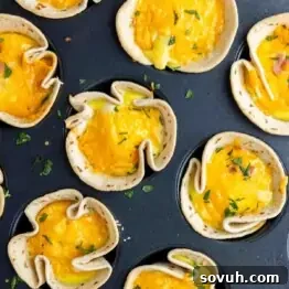 Muffin tin filled with easy breakfast burrito cups—tortilla shells holding a baked egg mixture, topped with melted cheese and sprinkled with herbs.