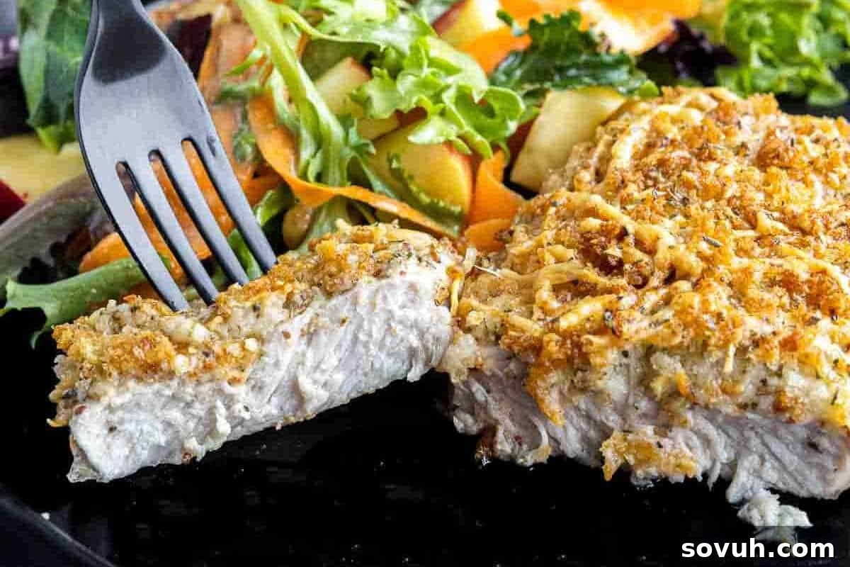 A fork holding a piece of crispy herb-crusted pork chop with a side of fresh salad with mixed greens and sliced vegetables.