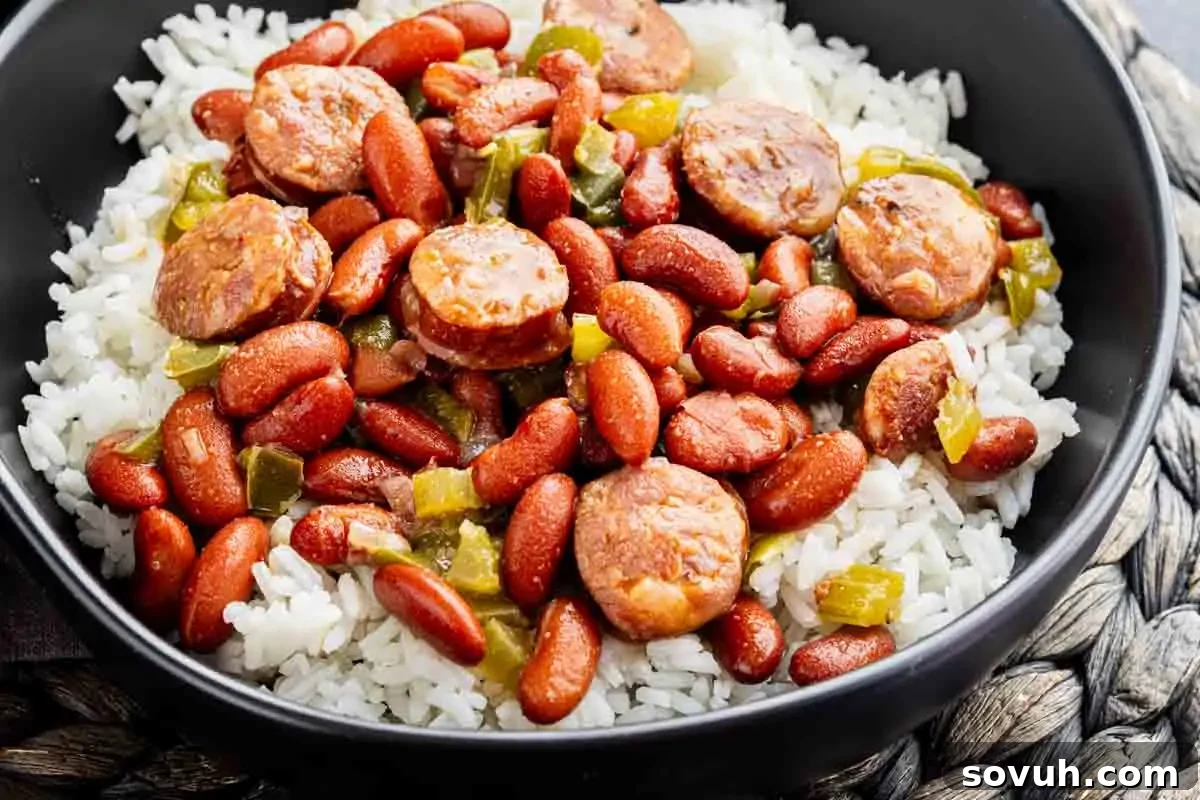 A bowl of white rice topped with red beans, sliced sausage, and green peppers.