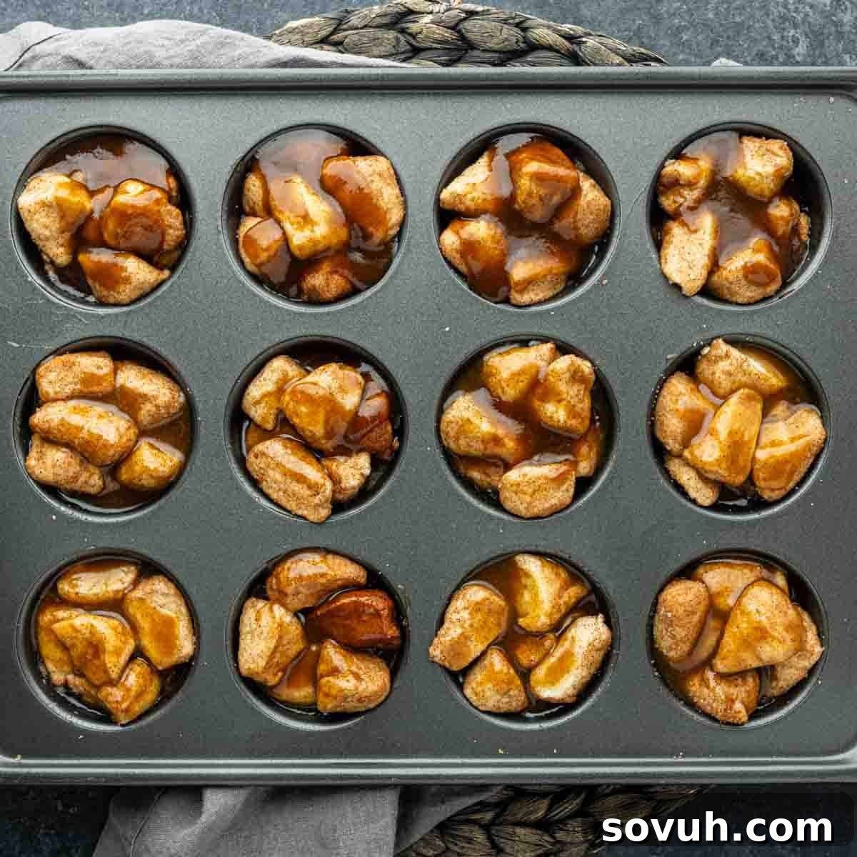 A muffin tin filled with unbaked cinnamon-sugar coated dough pieces topped with caramel sauce, these monkey bread muffins are ready to be baked for a sweet treat.