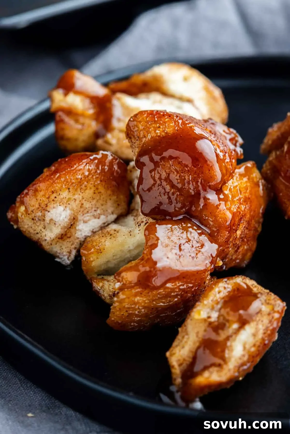 Close-up of monkey bread made with biscuits, drizzled with caramel sauce and served on a black plate.