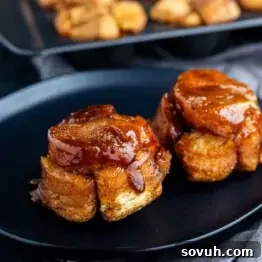 Two sticky, caramel-glazed monkey bread muffins are served on a black plate, with more muffins visible in the background.