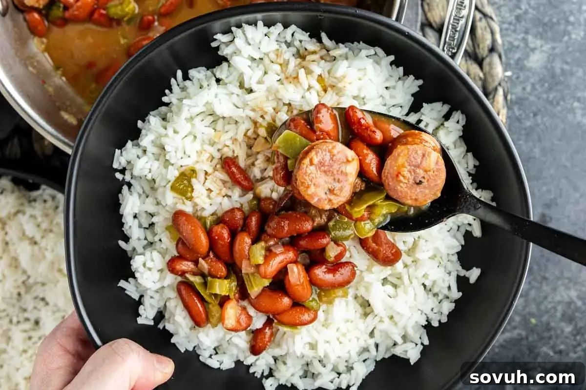 A bowl of white rice topped with red beans, sausage slices, and green peppers, with a spoon serving the mixture.