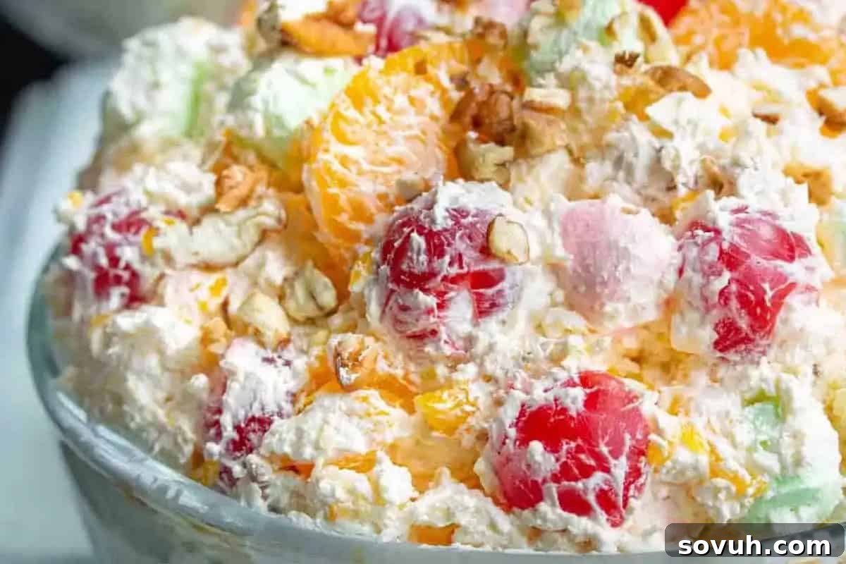 A bowl of ambrosia salad containing whipped cream, marshmallows, mandarin oranges, cherries, pineapple, and chopped nuts.