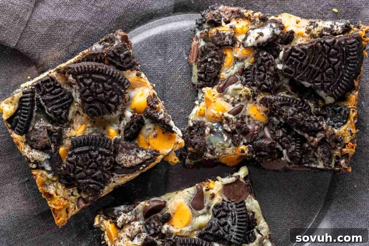 Three dessert bars topped with crushed chocolate sandwich cookies, chocolate chips, and butterscotch chips on a clear plate.