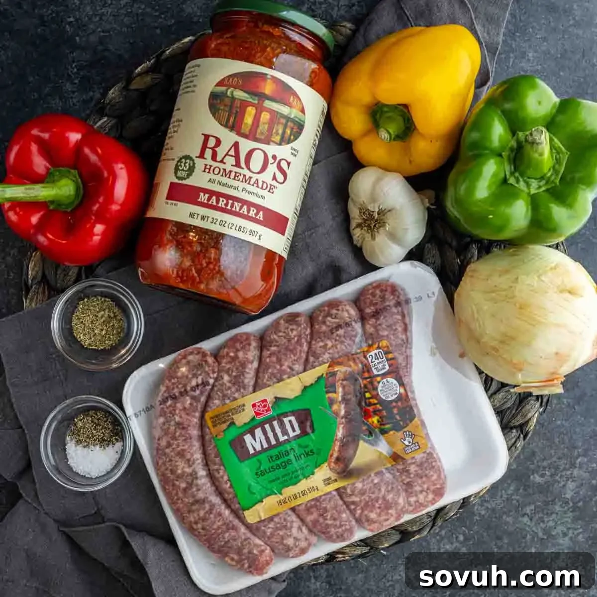 Ingredients for a meal: jar of Rao’s marinara sauce, bell peppers (red, yellow, green), garlic, onion, mild Italian sausage—perfect for making slow cooker sausage and peppers—plus salt and pepper on a dark surface.