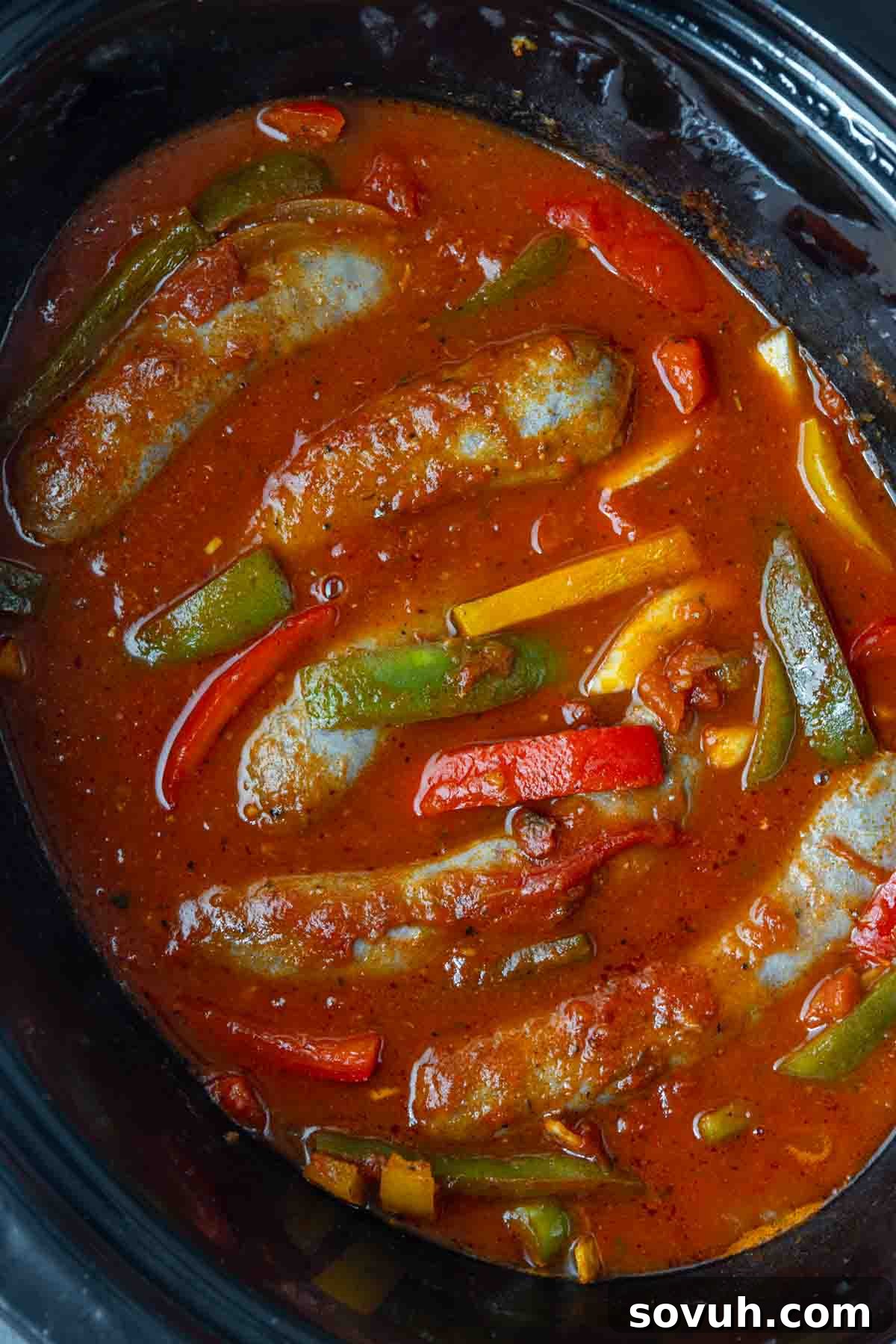 Sausages simmering in tomato sauce with sliced green, red, and yellow bell peppers make this classic slow cooker sausage and peppers dish a flavorful and easy meal.