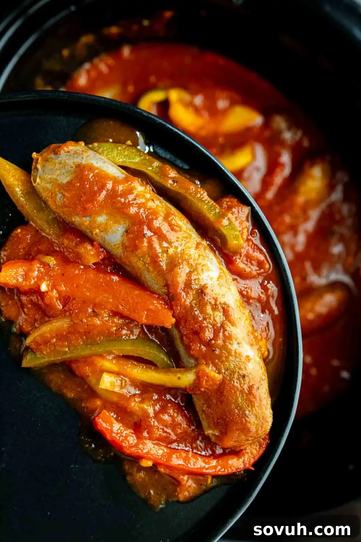 A cooked sausage with tomato sauce and sliced bell peppers served in a black bowl, just like classic slow cooker sausage and peppers.