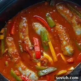 Sausages simmering in a tomato-based sauce with sliced red, yellow, and green bell peppers in a pot.