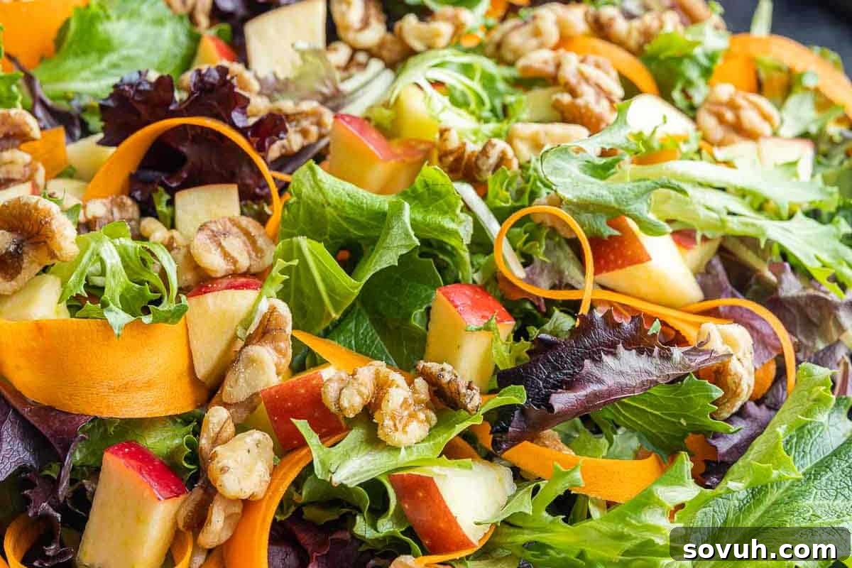 A vibrant, fresh salad featuring a medley of mixed greens, perfectly sliced carrots, crisp red and green apple pieces, and crunchy walnuts, all artfully arranged for a delightful fall recipe.