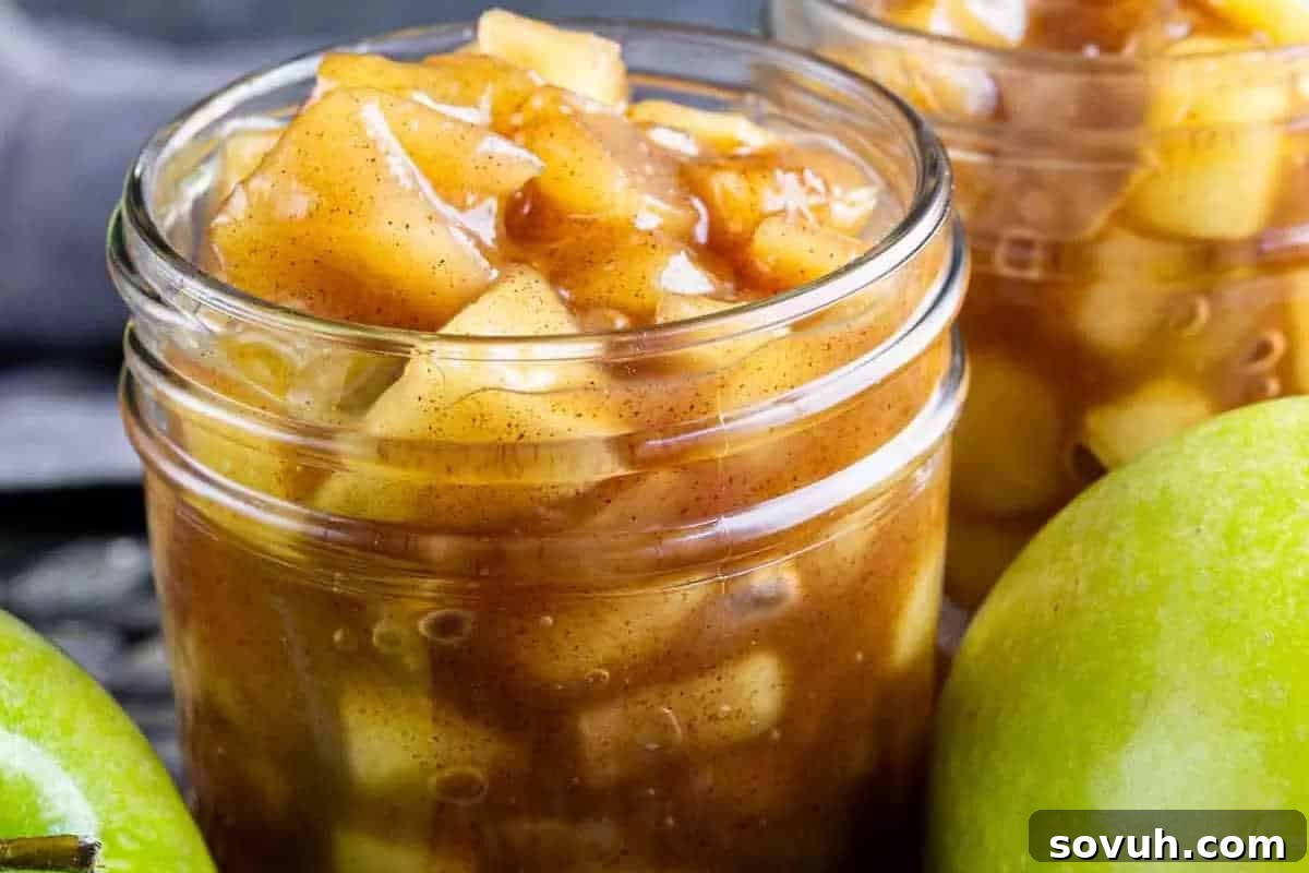 A beautifully clear glass jar filled with chunky, spiced apple pie filling, ready to be used in delicious fall recipes, with fresh green apples visibly placed in the foreground, highlighting the natural ingredients.