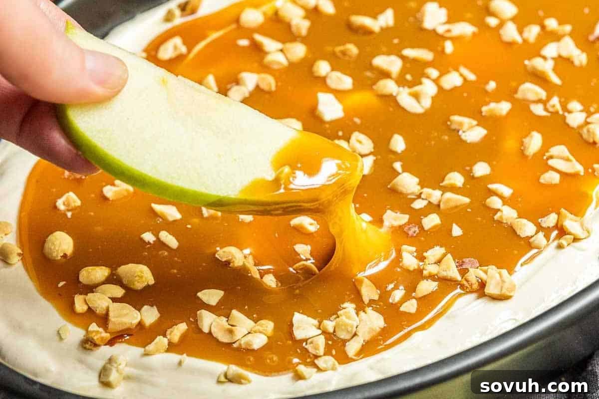 A vibrant green apple slice poised to be dipped into a luscious caramel sauce, lavishly topped with finely chopped nuts, showcasing a perfect sweet treat for apple enthusiasts and fall dessert lovers.
