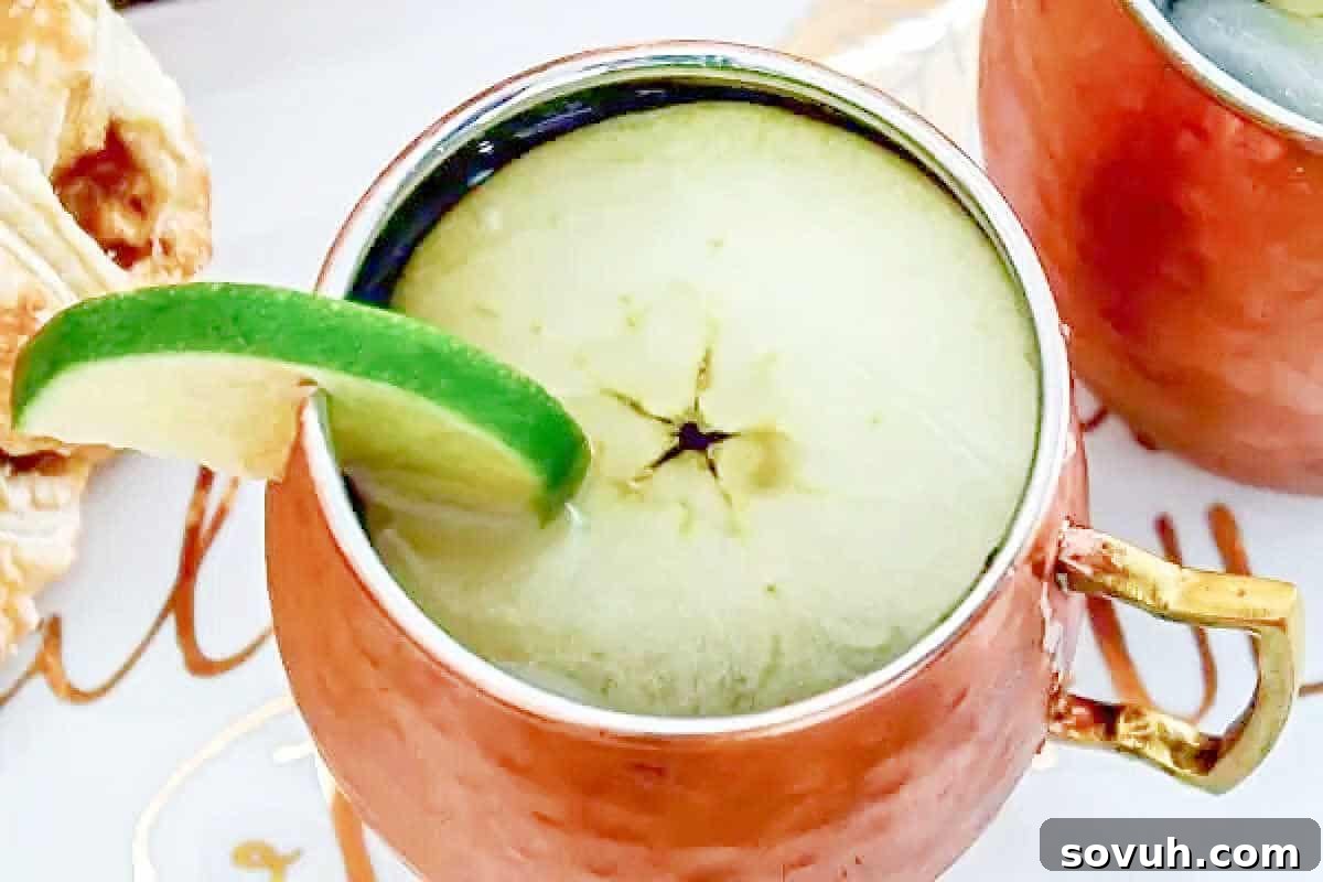 A gleaming copper mug brimming with a refreshing drink, elegantly garnished with a delicate thin apple slice and a vibrant lime wedge perched on the rim, a perfect cocktail for cozy fall recipes and apple lovers.