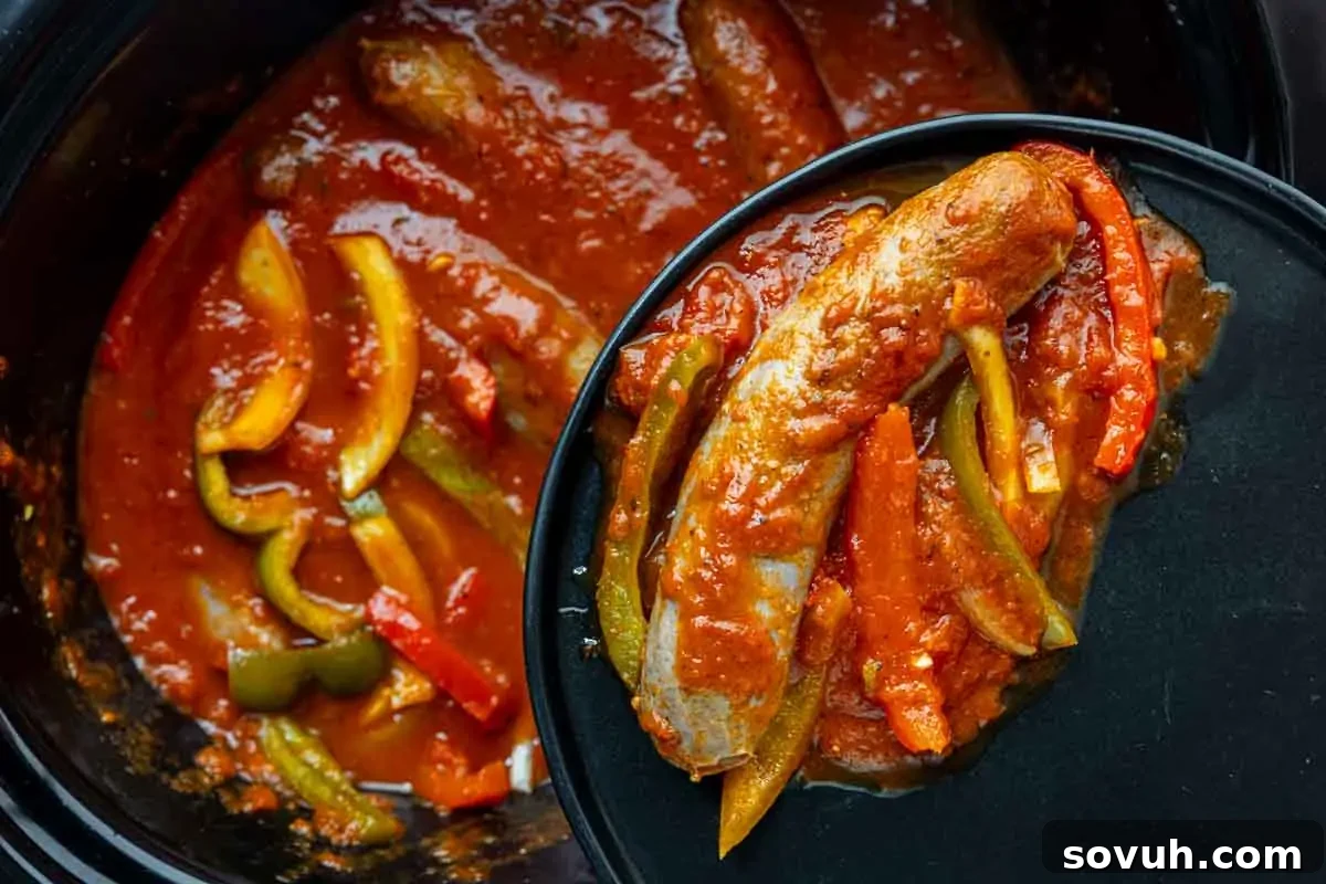 Hearty slow cooker sausage and peppers with rich tomato sauce and bell peppers, served on a black plate, a perfect fall comfort food.