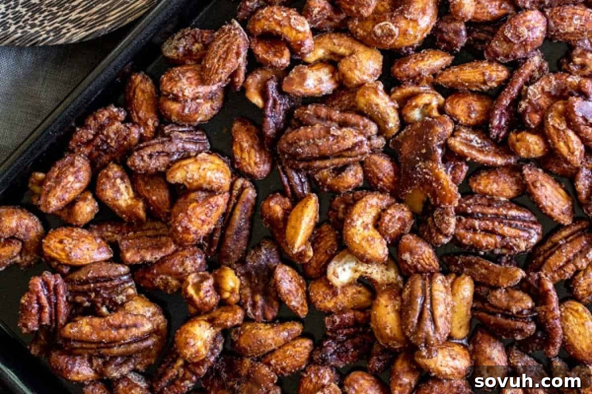 A close-up of assorted slow cooker spiced nuts, including pecans, cashews, and almonds, spread on a baking sheet, ideal for cozy fall snacking.