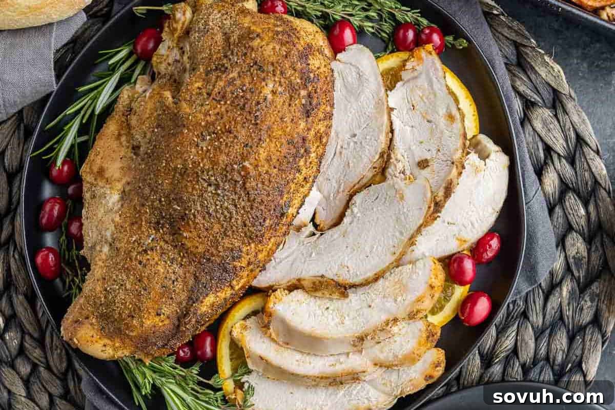 A beautifully presented dish of sliced roasted Slow Cooker Turkey Breast, garnished with rosemary, orange slices, and cranberries on a black plate.