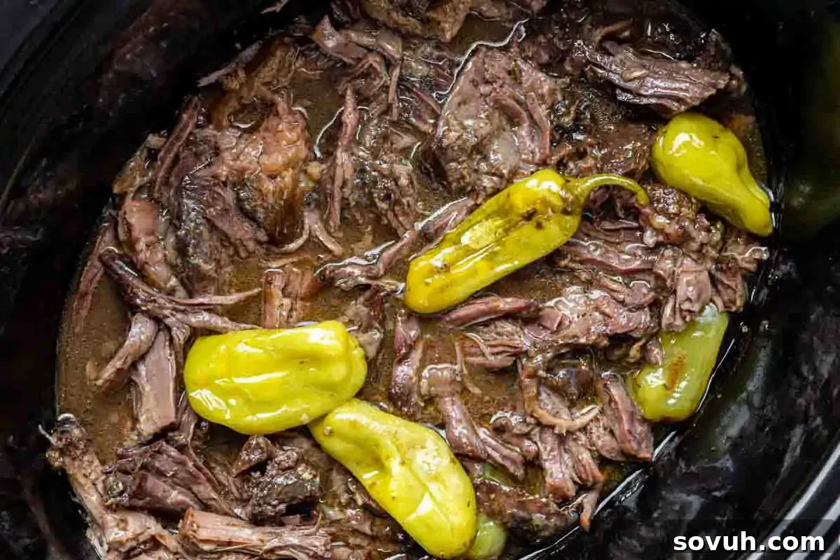 Tender shredded Slow Cooker Mississippi Pot Roast, topped with whole yellow peppers, nestled in a black slow cooker, a perfect fall family dinner.