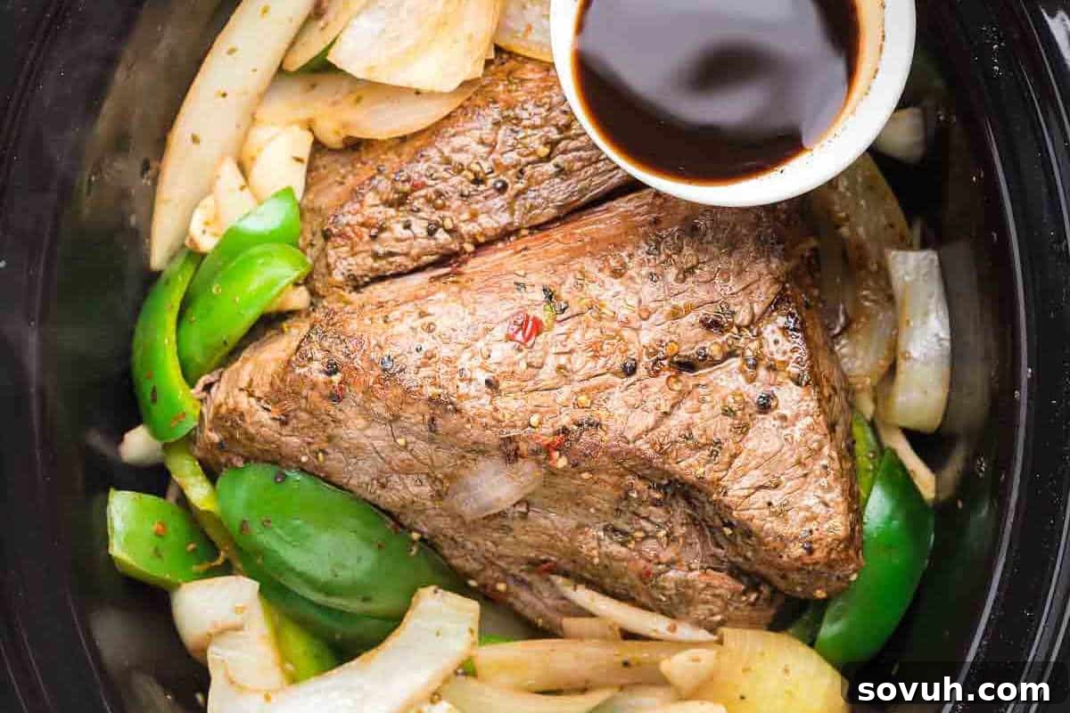 Slow-cooked, seasoned Crock Pot Italian Beef with vibrant green bell peppers and onions, served with a side of savory jus.