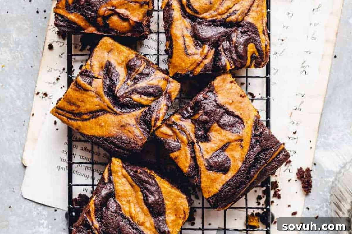 Marbled chocolate and pumpkin brownies on a cooling rack, with pages underneath on a light surface.