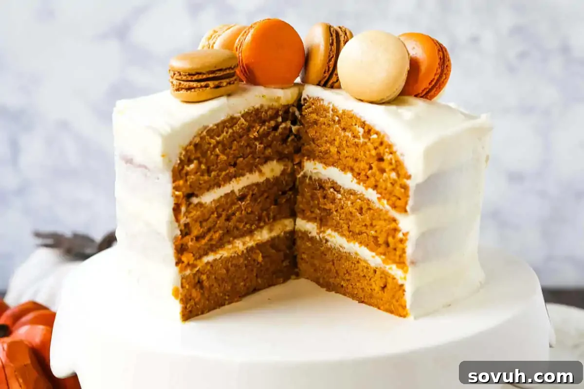 A three-layer cake with white frosting, topped with assorted macarons, partially sliced, on a white cake stand.