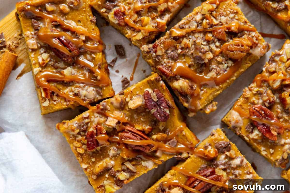 Caramel drizzled pumpkin bars topped with chopped nuts and pecans on a parchment-lined surface.