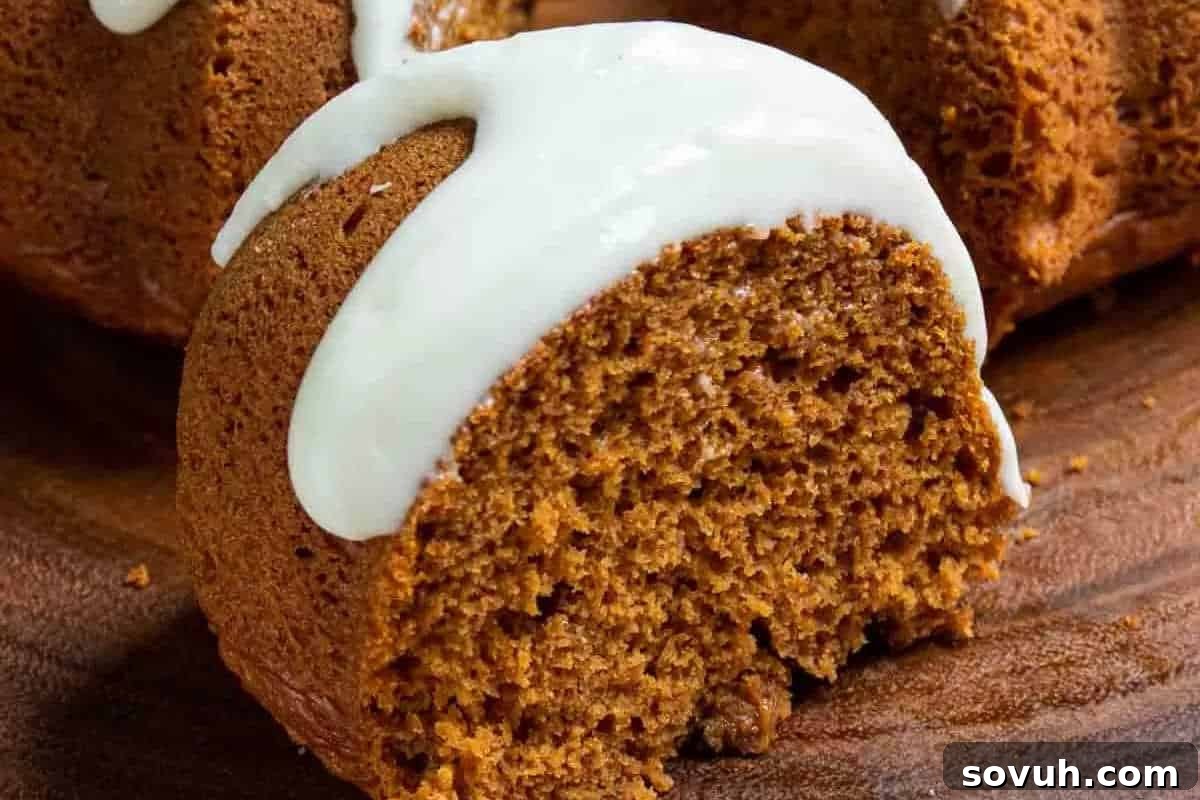 A slice of brown bundt cake with white icing on top, resting on a wooden surface.