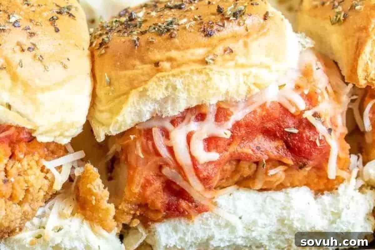 Three chicken parmesan sliders with melted cheese and marinara sauce served on fluffy buns with sprinkled herbs.