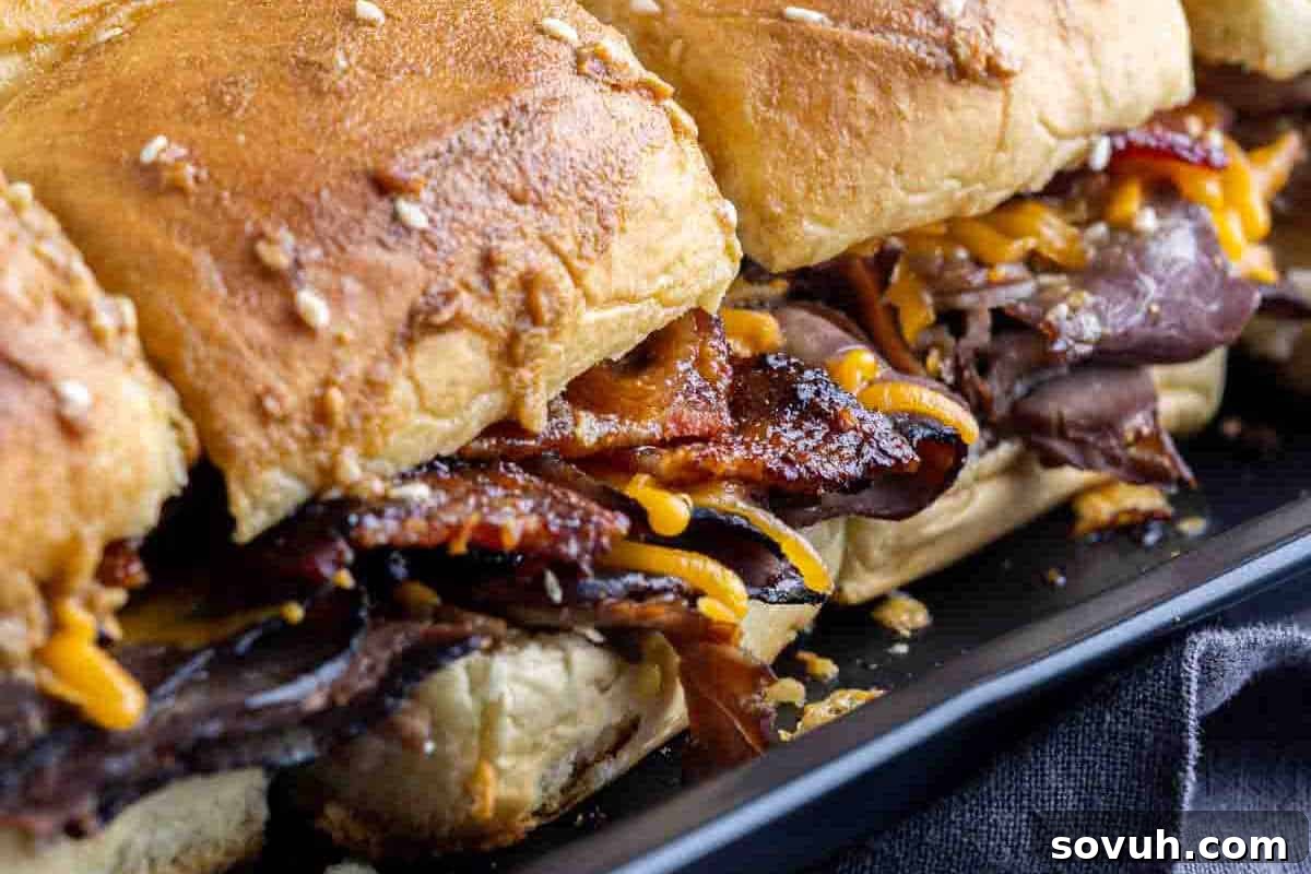Close-up of a sandwich with sesame seed buns, filled with melty cheese, and crispy bacon.