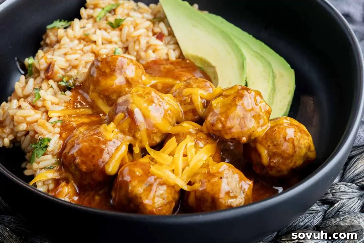 A black bowl with rice, sliced avocado, and meatballs topped with shredded cheese and sauce.