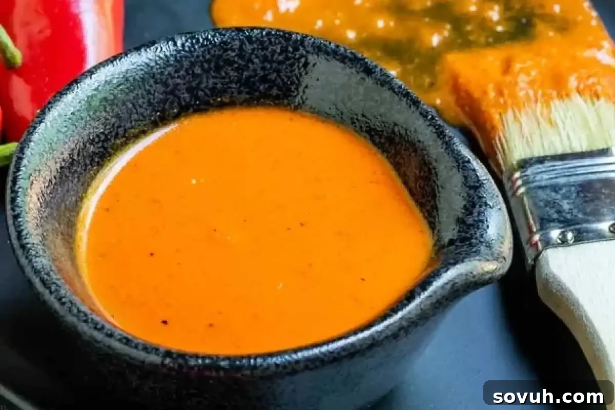 A black bowl filled with homemade orange-red Piri Piri Sauce, a traditional Portuguese chili sauce, with a basting brush on a dark surface.