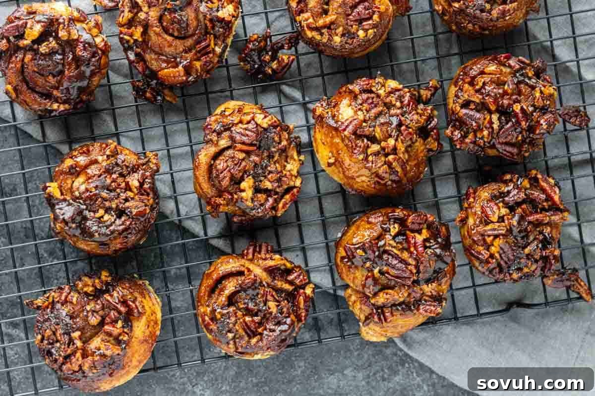Twelve golden sticky buns with caramelized pecans cooling on a black wire rack, glistening with a sweet glaze.