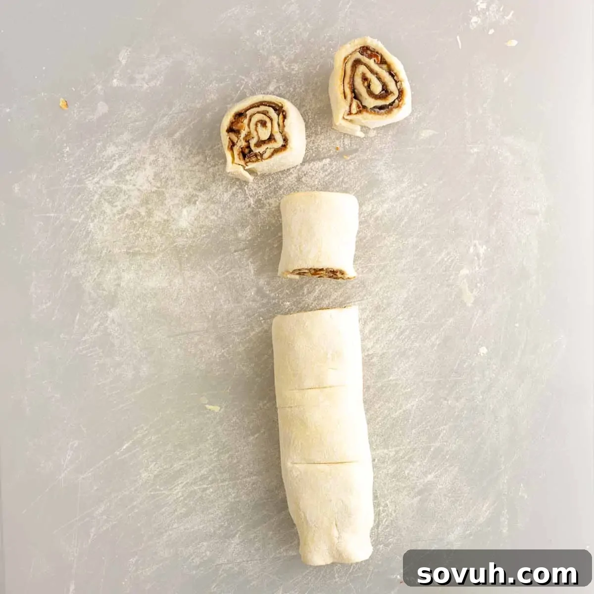 A rolled log of sticky bun dough, partially sliced to show the inner spiral, on a floured surface.